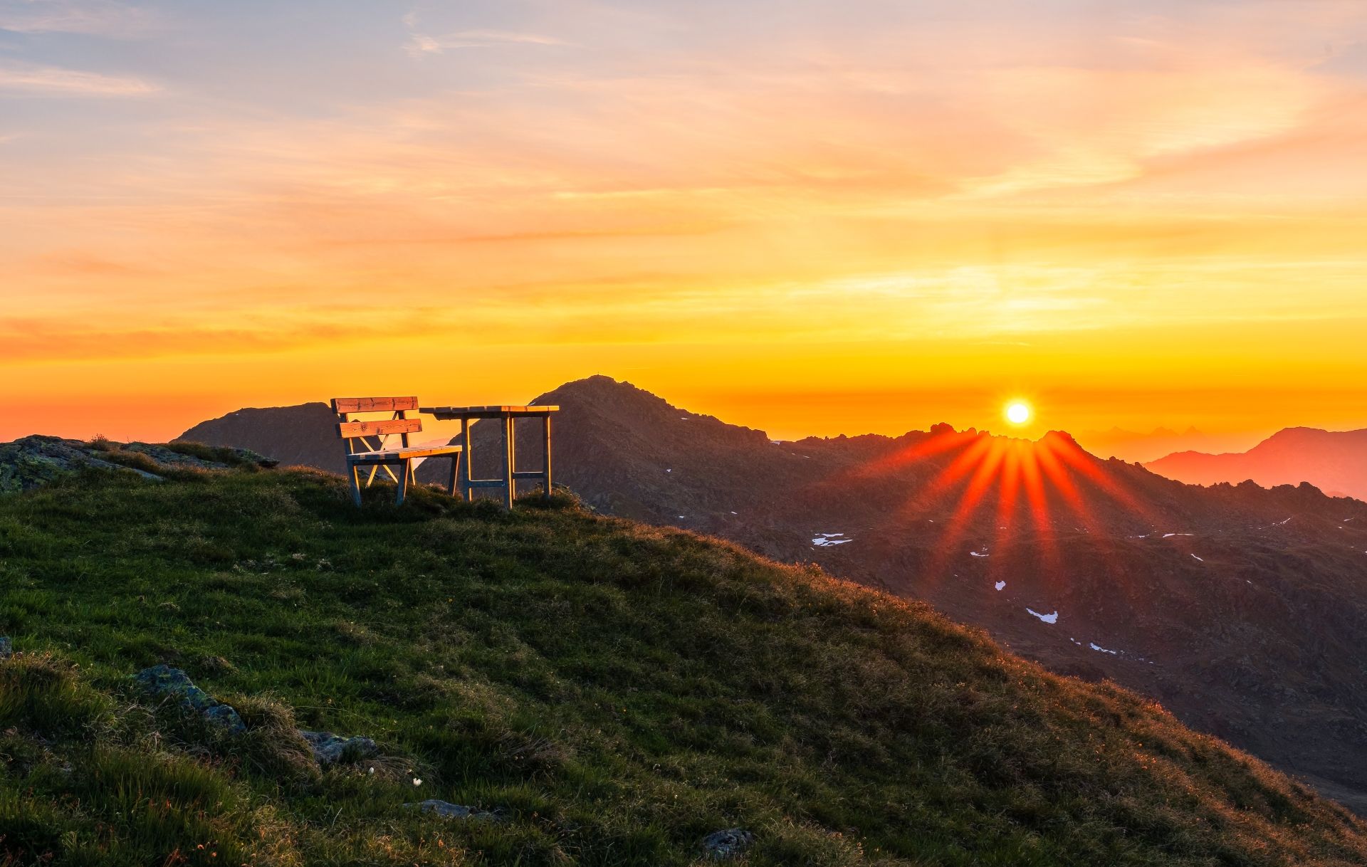 Sonnenaufgang Rifflerkogl Vorne der Gipfel des Rifflerkogl mit einem Tisch und einer Bank zum Sitzen im Hintergrund der Sonnenaufgang