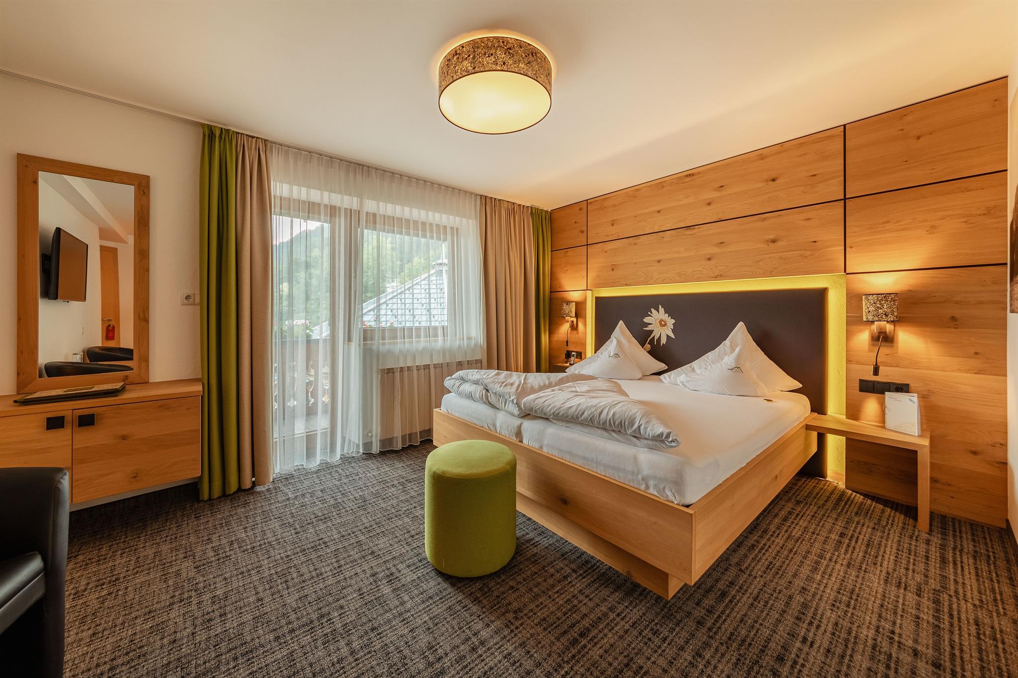 Modern hotel room with a double bed, wooden wall panels, window with curtains, and bedside lamps.