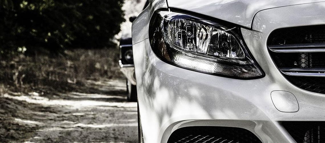 Close-up of a white car on a dirt road, focusing on the front right side and headlight.