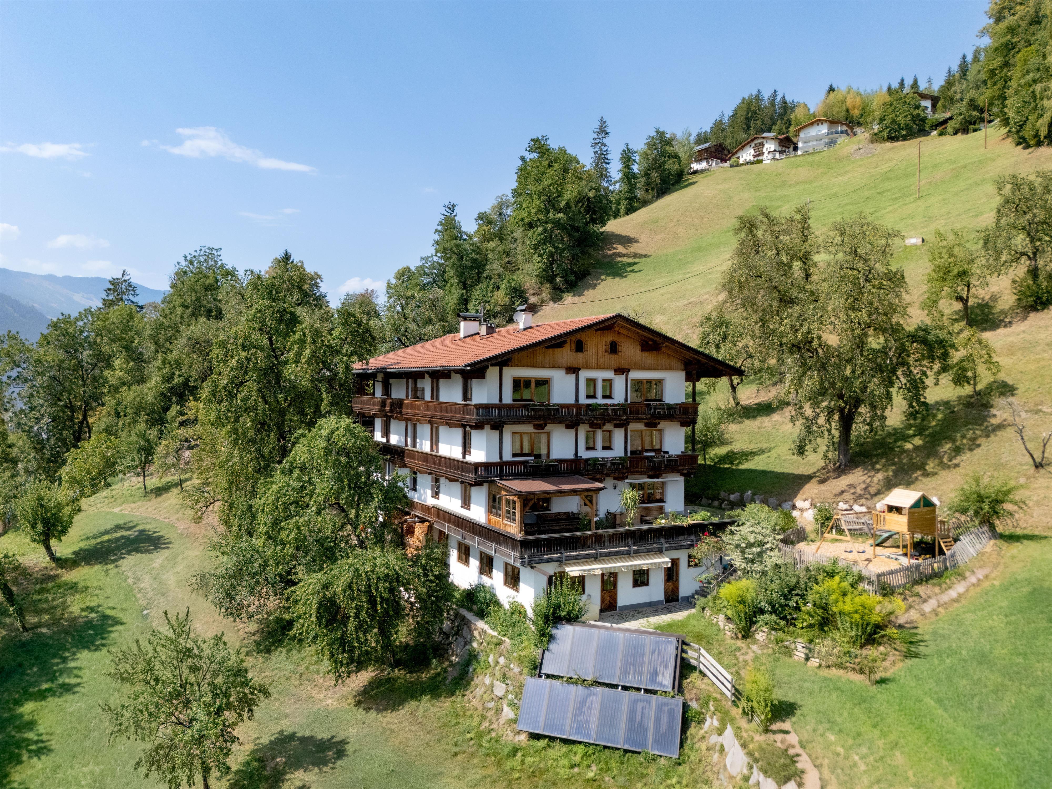Houses on a hillside with trees and blue sky, in a rural alpine area.