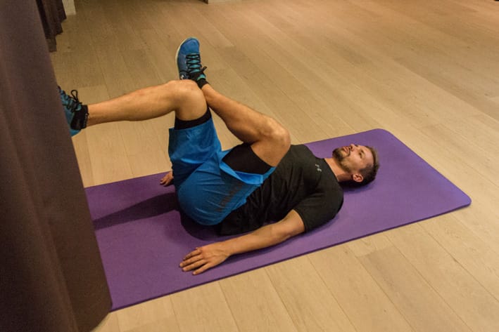 Man lying on yoga mat stretching lower back against wall in training room in Mayrhofen. Christoph Ebenbichler demonstrates an effective lumbar stretch for ski fitness and recovery.