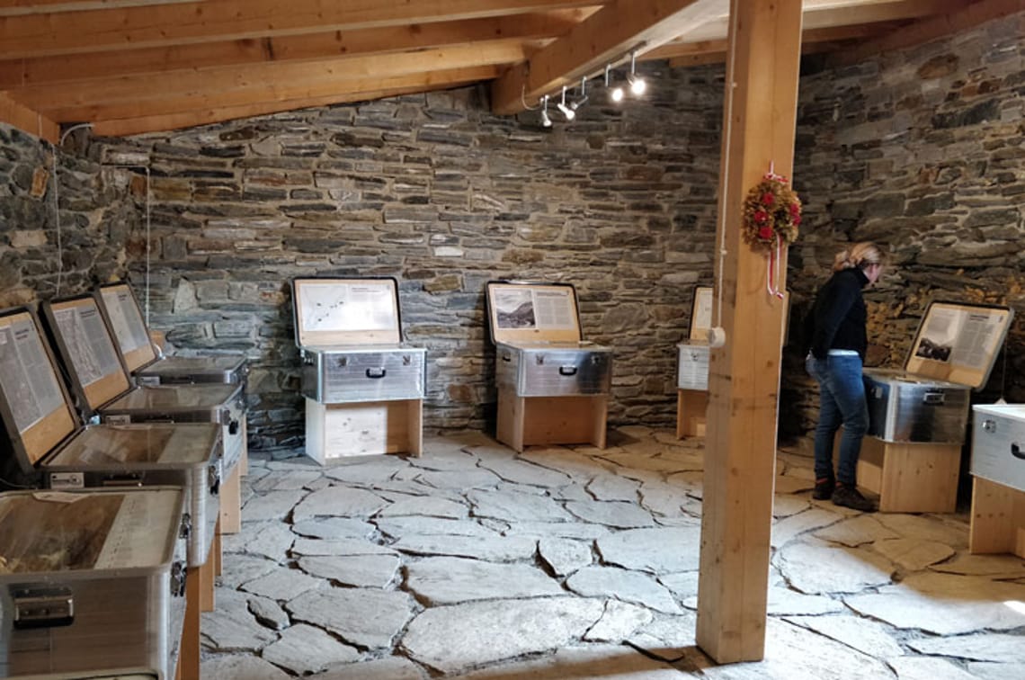 Ausstellung "Pfitscher Joch grenzenlos" Innenansicht der Naturpark Ausstellung "Pfitscher Joch grenzenlos" auf der Lavitzalm im Zillertal: Raum mit Steinboden, Holzbalken und Schautafeln zur Geschichte des alpinen Übergangs seit der Steinzeit.