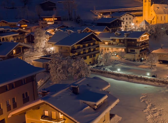 Night view of snow-covered houses and a church in a winter village, warm lights glow from the windows.