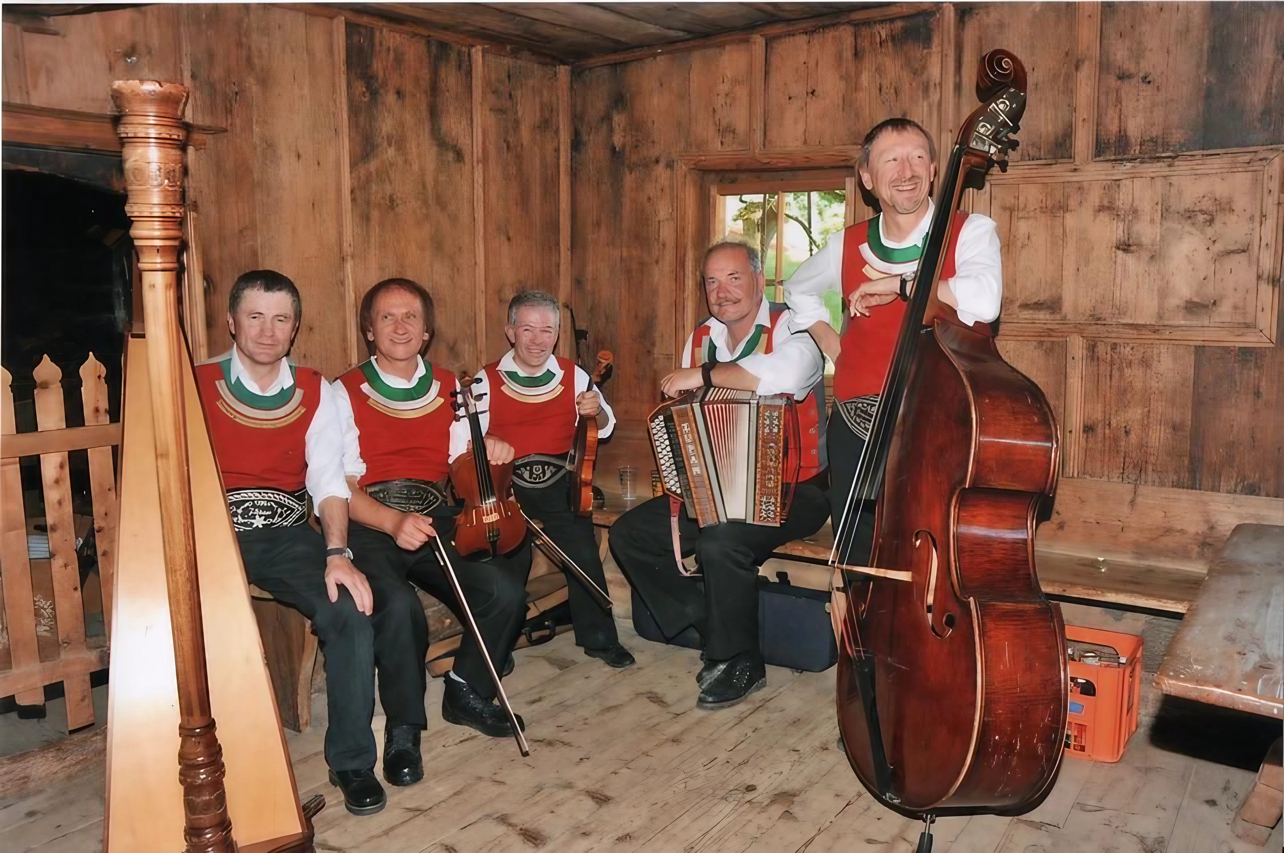 The image shows the musicians of the Schwendberger Geigenmusik with instruments in a rustic farmhouse room.
