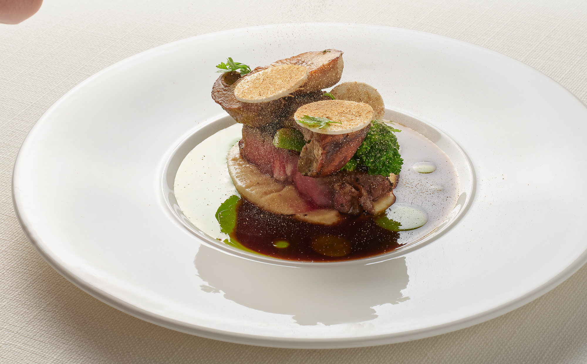 Nahaufnahme eines edlen Gourmet-Gerichts im Restaurant Kle. Fein angerichtete Komponenten mit Schaum und frischen Kräutern auf einem dunklen, rustikalen Keramikteller, serviert auf einem dunklen Holztisch.