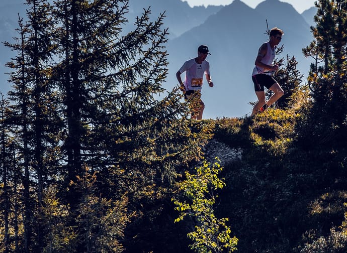 Zwei Läufter hinter Bäumen und vor einer Bergkulisse