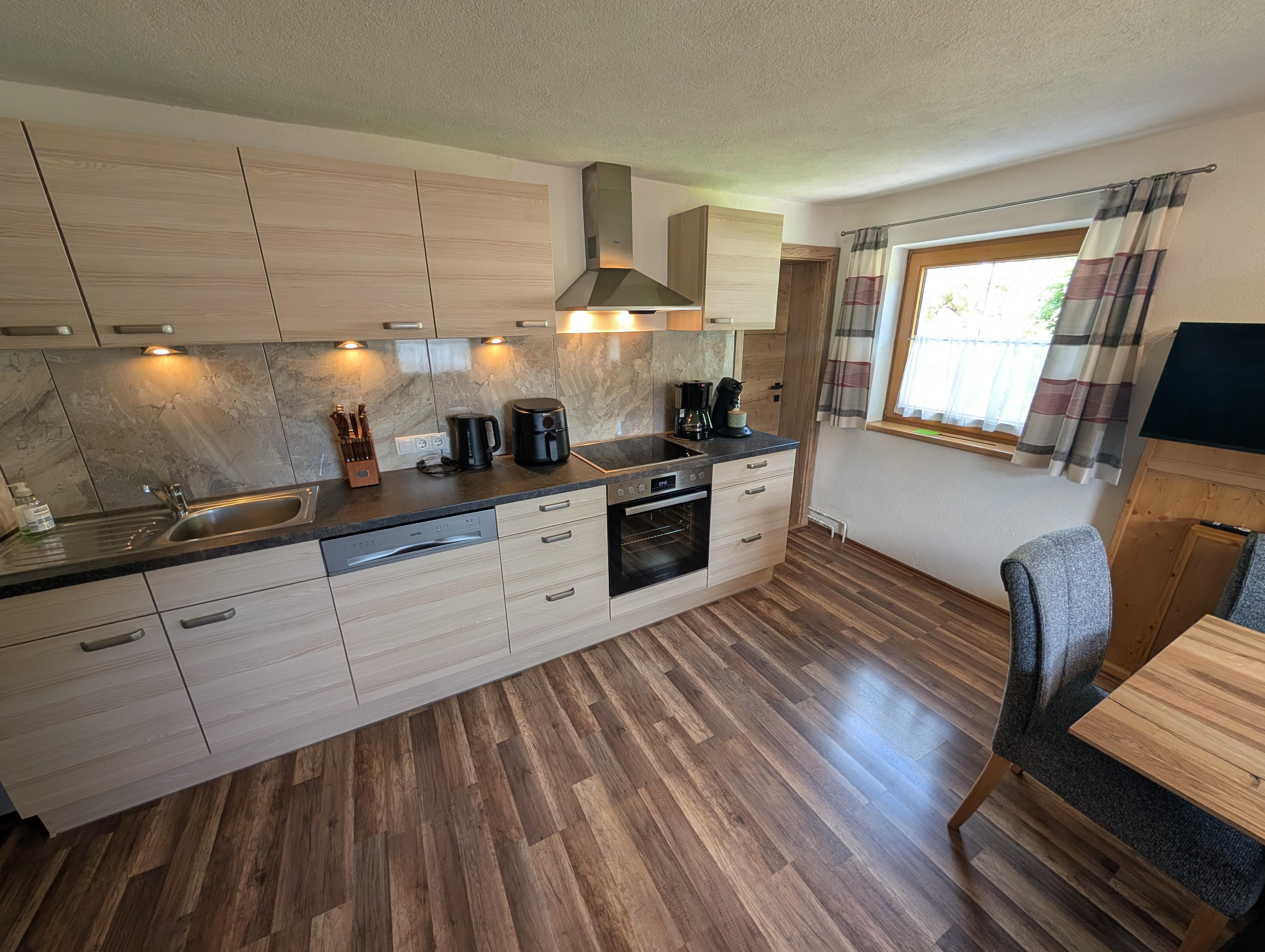 Küche mit Holzkabelfronten, Herd, Dunstabzug, Kaffeemaschine und Fenster mit Vorhängen, Holzfußboden.