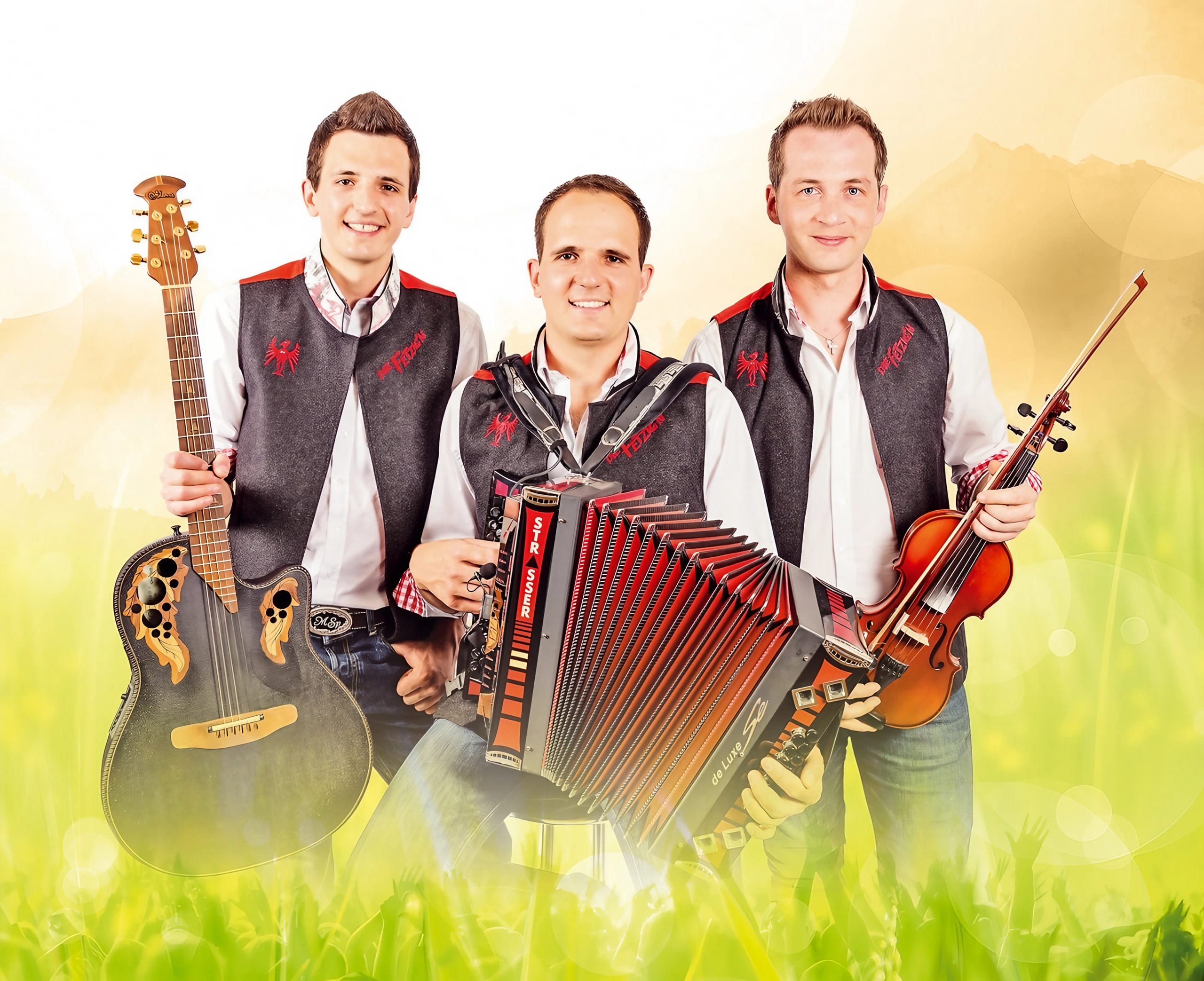Drei Männer in Trachten mit Musikinstrumenten, lachend vor gelbem Hintergrund, feiern gemeinsam.