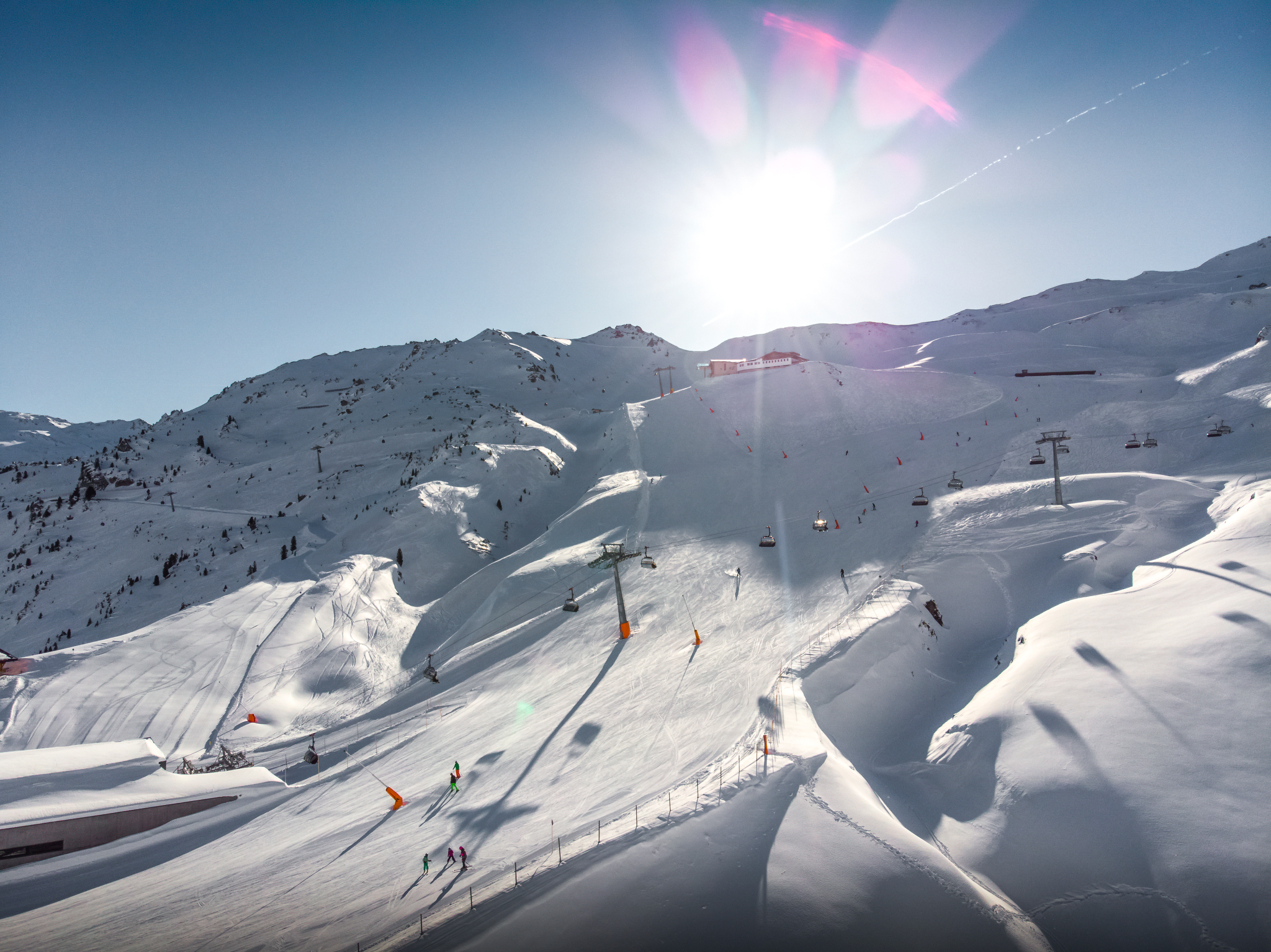 Schneebedeckte Berge mit Skiliften, Skifahrern und Sonnenschein am klaren Himmel.