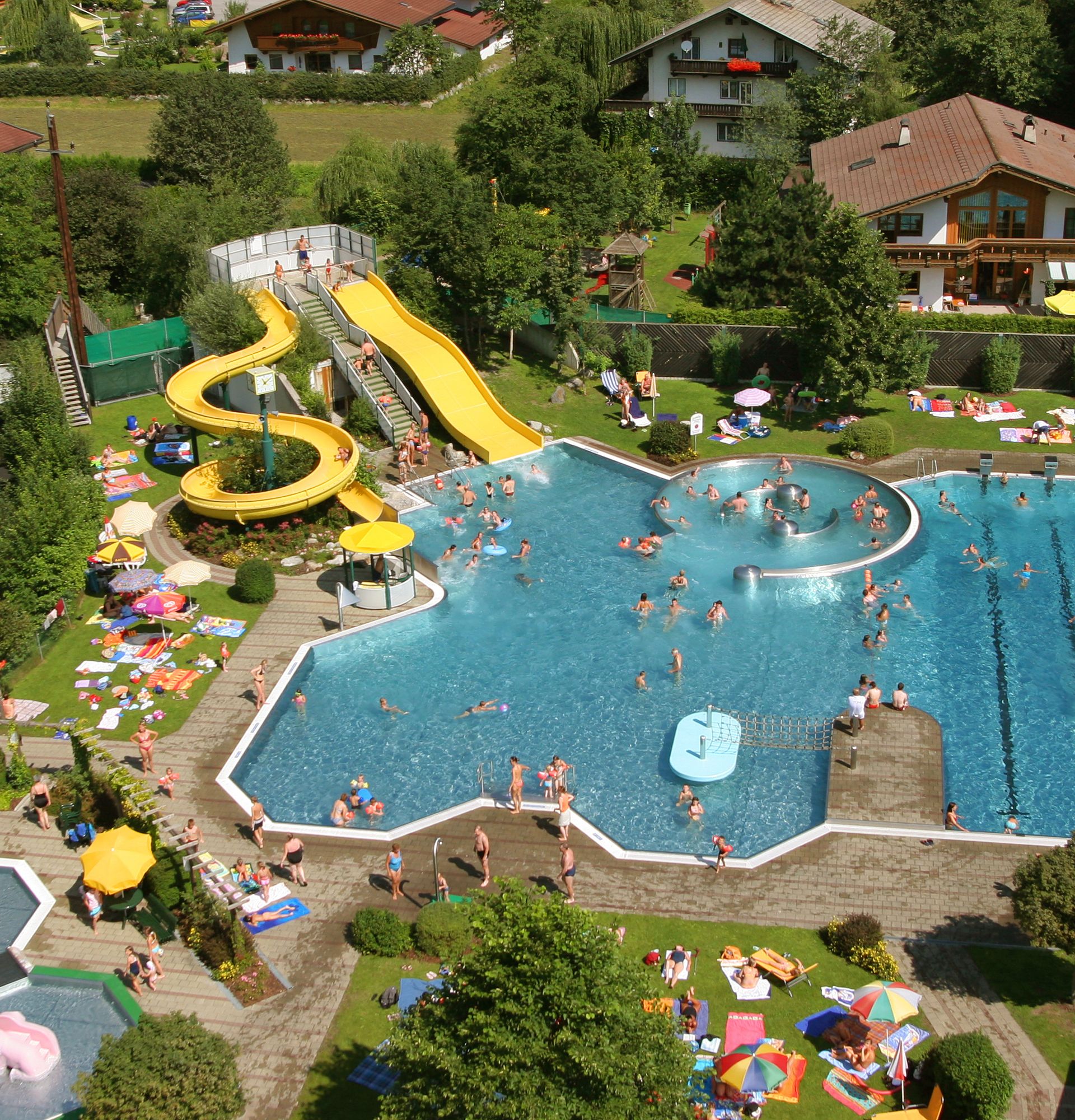 Aerial view of the outdoor swimming pool at Sommerwelt Hippach in the Zillertal valley with water slide, children's area, sports pool, and sunbathing lawn – a popular destination for families and swimming enthusiasts in Tyrol.