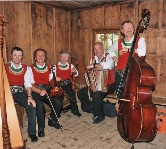 The image shows the musicians of the Schwendberger Geigenmusik with instruments in a rustic farmhouse room.