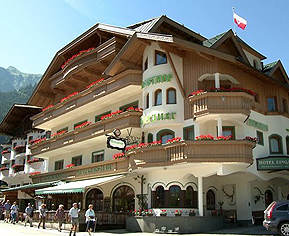 Das Bild zeigt den Gasthof Perauer von außen. Über dem Gebäude erstreckt sich ein klarer blauer Himmel, der der Szenerie eine freundliche und helle Stimmung verleiht.