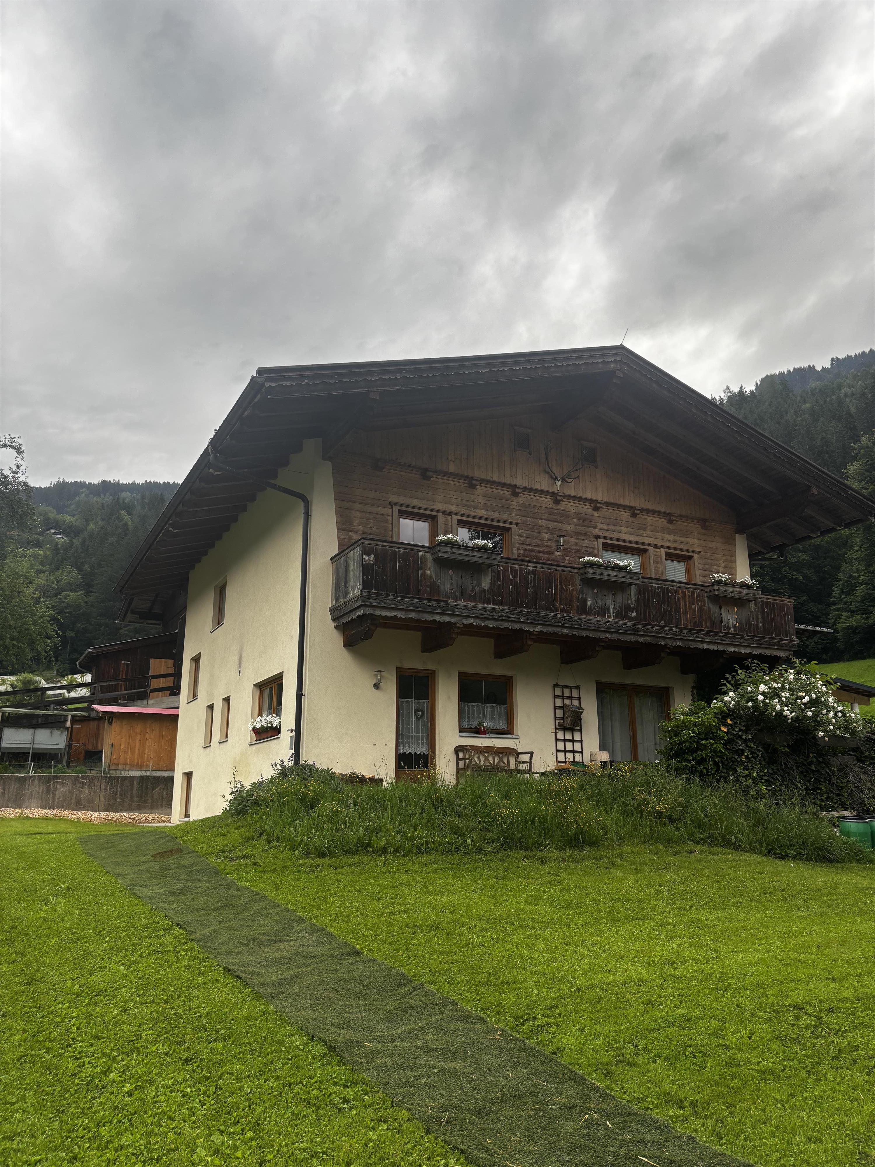 Ein zweistöckiges Haus mit Holz- und Putzfassade, Balkon und Garten, bei bewölktem Himmel im Grünen.