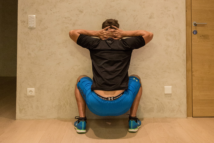 Mann macht Wall Squats an der Wand in Trainingsraum in Mayrhofen. Christoph Ebenbichler zeigt effektive Übung zur Stärkung von Beinen und Rumpf für die Skivorbereitung – fit in den Winter starten.