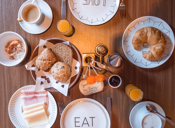 Frühstückstisch mit Croissants, Kaffee, Orangensaft und Brotsorten auf Tellern und Tassen, mit