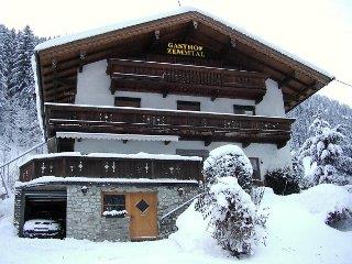 The picture shows Gasthof Zemmtal from the outside in winter. A car is parked in the garage, and in the background, a snowy forest stretches out, emphasizing the wintry atmosphere.