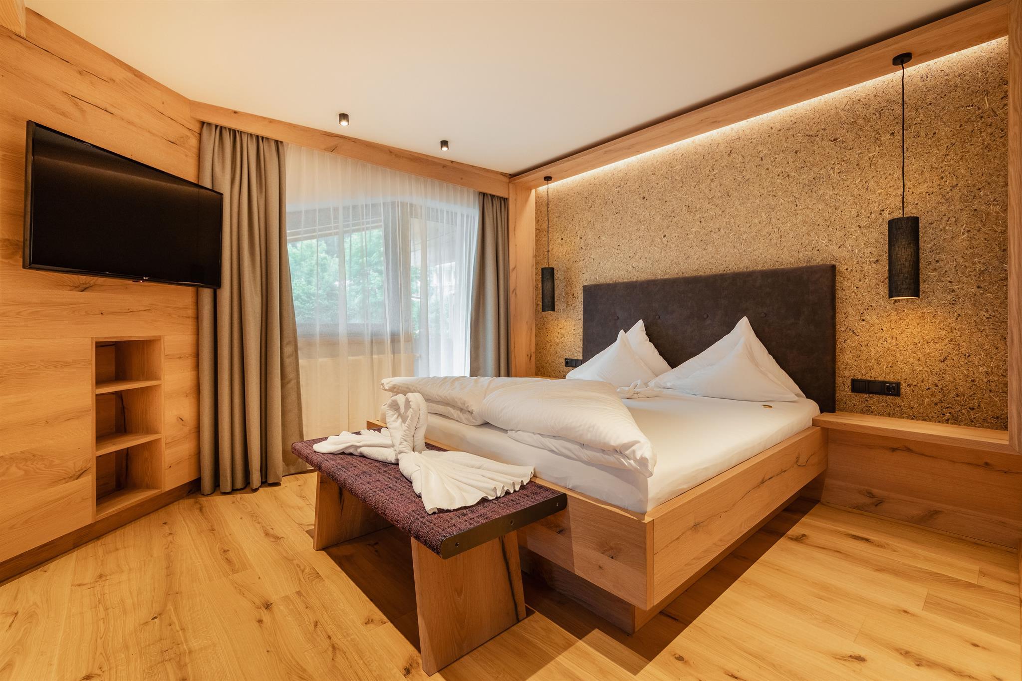 Modern bedroom with wooden decor, bed, curtains, TV, and warm lighting, cozy and stylish.
