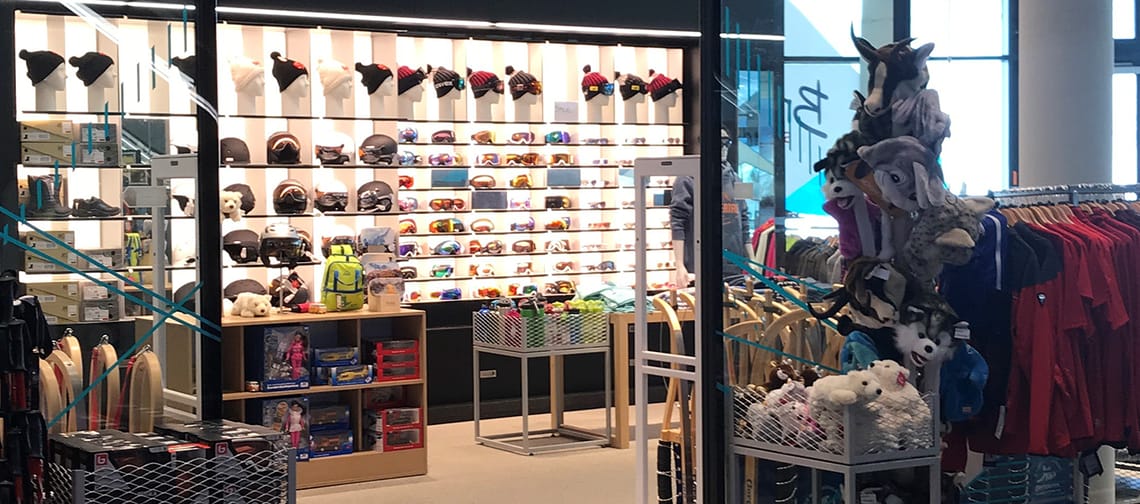 Innenansicht des Bründl-Sport-Shops an der Talstation Penken in Mayrhofen. Links und rechts hängen Jacken und Sportbekleidung, mittig ein heller Verkaufsbereich mit Regalen und beleuchteter Warenpräsentation. Moderne, übersichtliche Ladenstruktur.