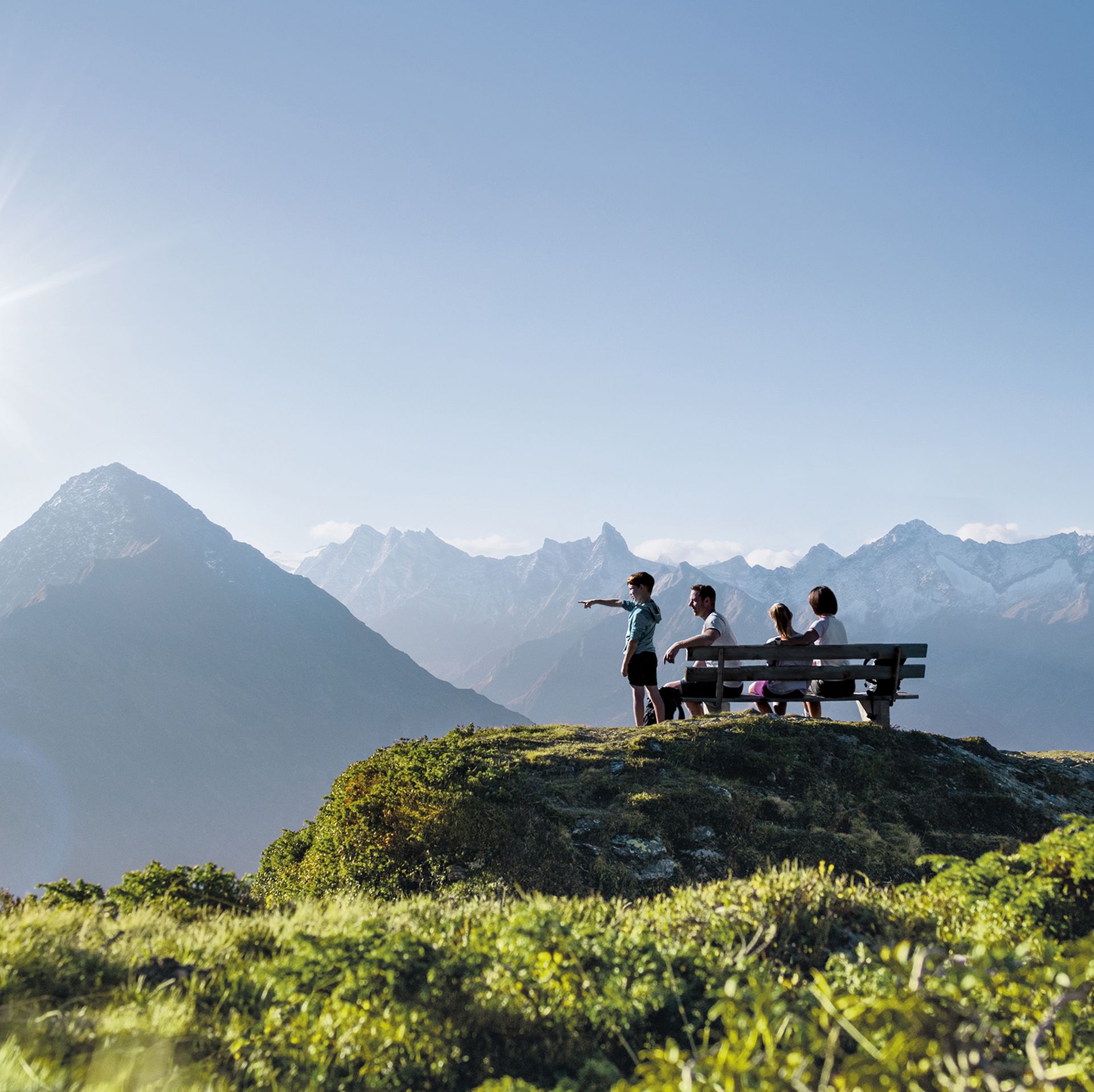 Gruppe auf einer Aussichtsplattform in den Zillertaler Alpen. Sonniger Tag, grüne Wiesen, beeindruckende Bergkulisse mit schneebedeckten Gipfeln im Hintergrund.