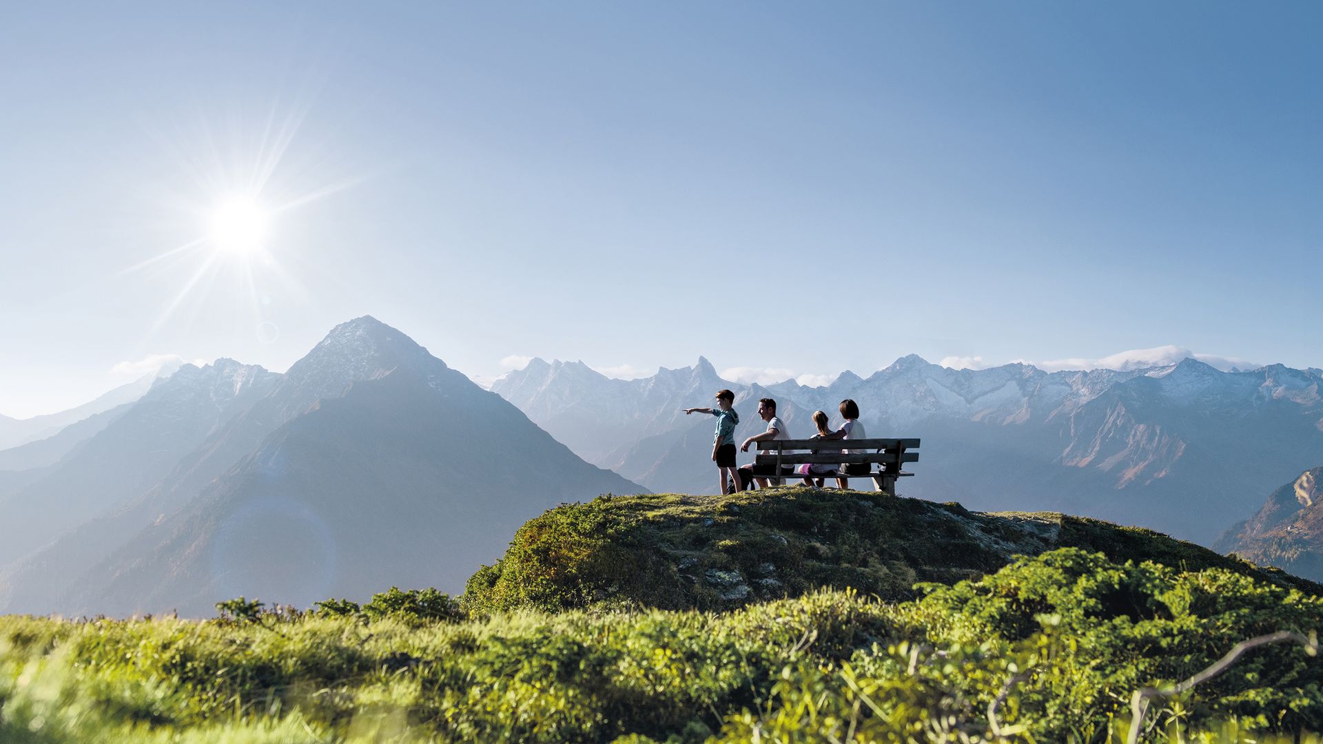 Gruppe auf einer Aussichtsplattform in den Zillertaler Alpen. Sonniger Tag, grüne Wiesen, beeindruckende Bergkulisse mit schneebedeckten Gipfeln im Hintergrund.