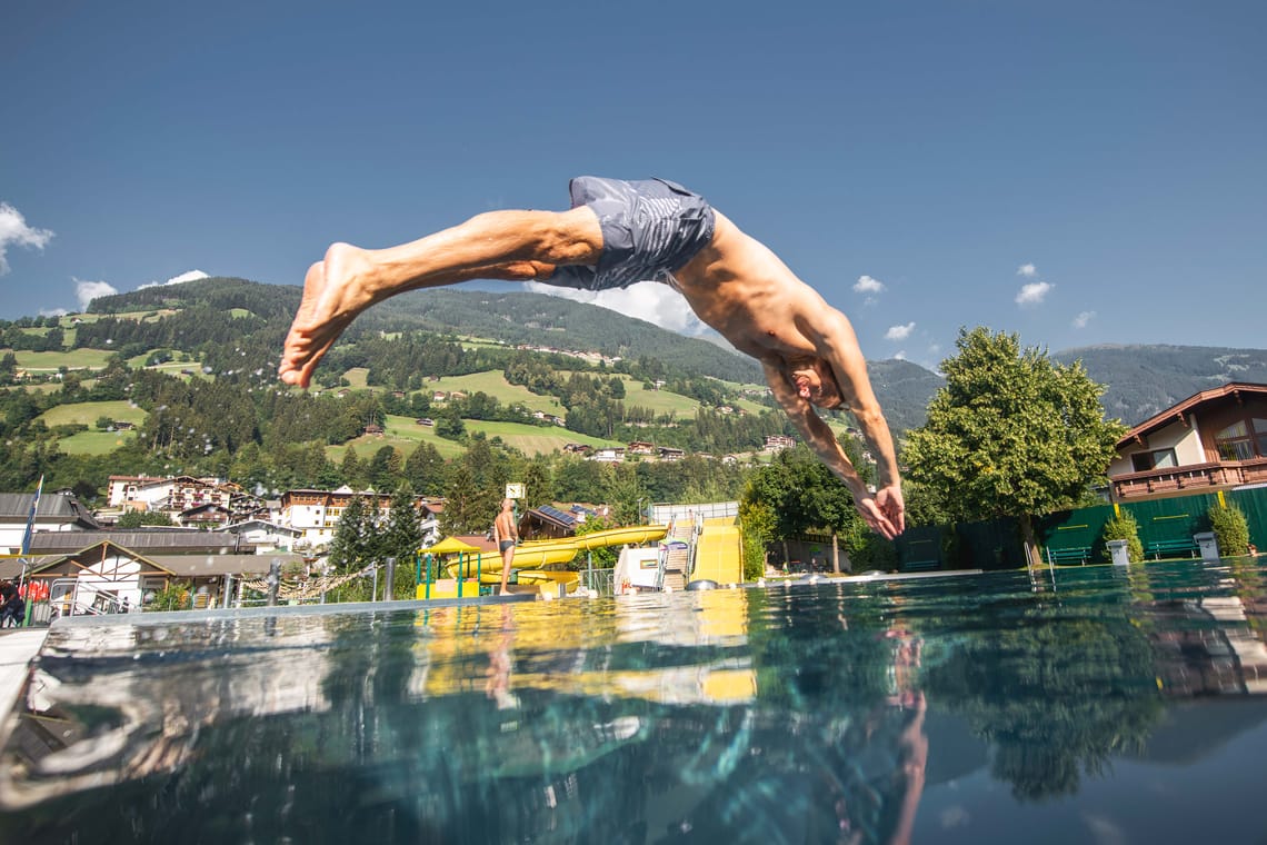 Freischwimmbad Hippach - Sprung ins Wasser Freischwimmbad Hippach – Mann springt ins Wasser vor alpiner Kulisse bei strahlendem Sonnenschein. Sommerlicher Badespaß, Bewegung und Natur im Zillertal, Tirol.