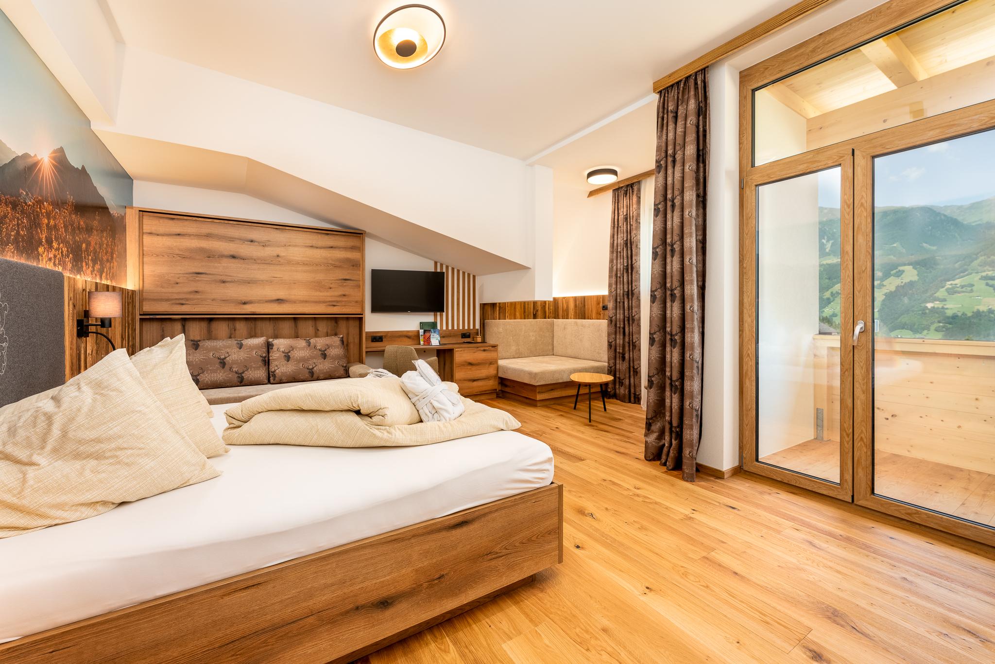 A modern hotel room with wooden decor, large windows, and mountain view outside.
