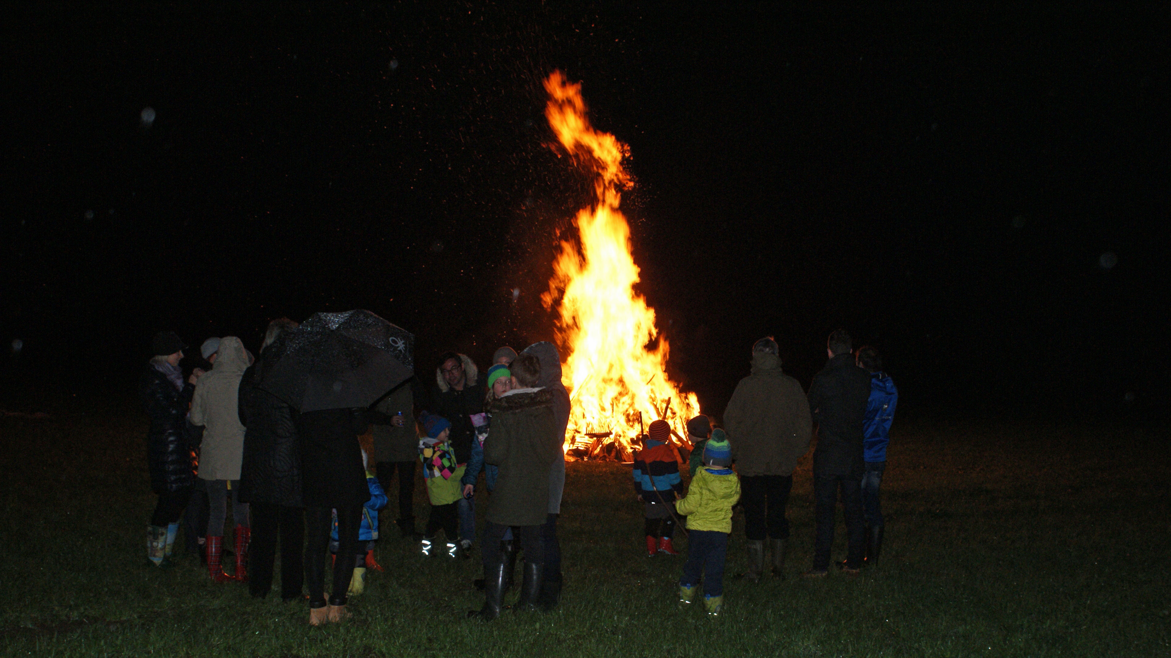 Menschen stehen in einem Kreis um ein hell loderndes Osterfeuer in Mayrhofen, Zillertal. Groß und Klein blicken in die Flammen, die die dunkle Nacht erhellen. Der traditionelle Brauch bringt die Gemeinschaft zusammen.