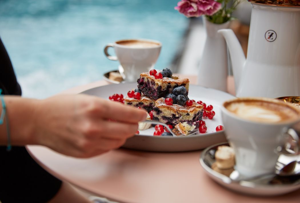 Person is cutting a berry cake with a fork on a plate, with coffee in the background.
