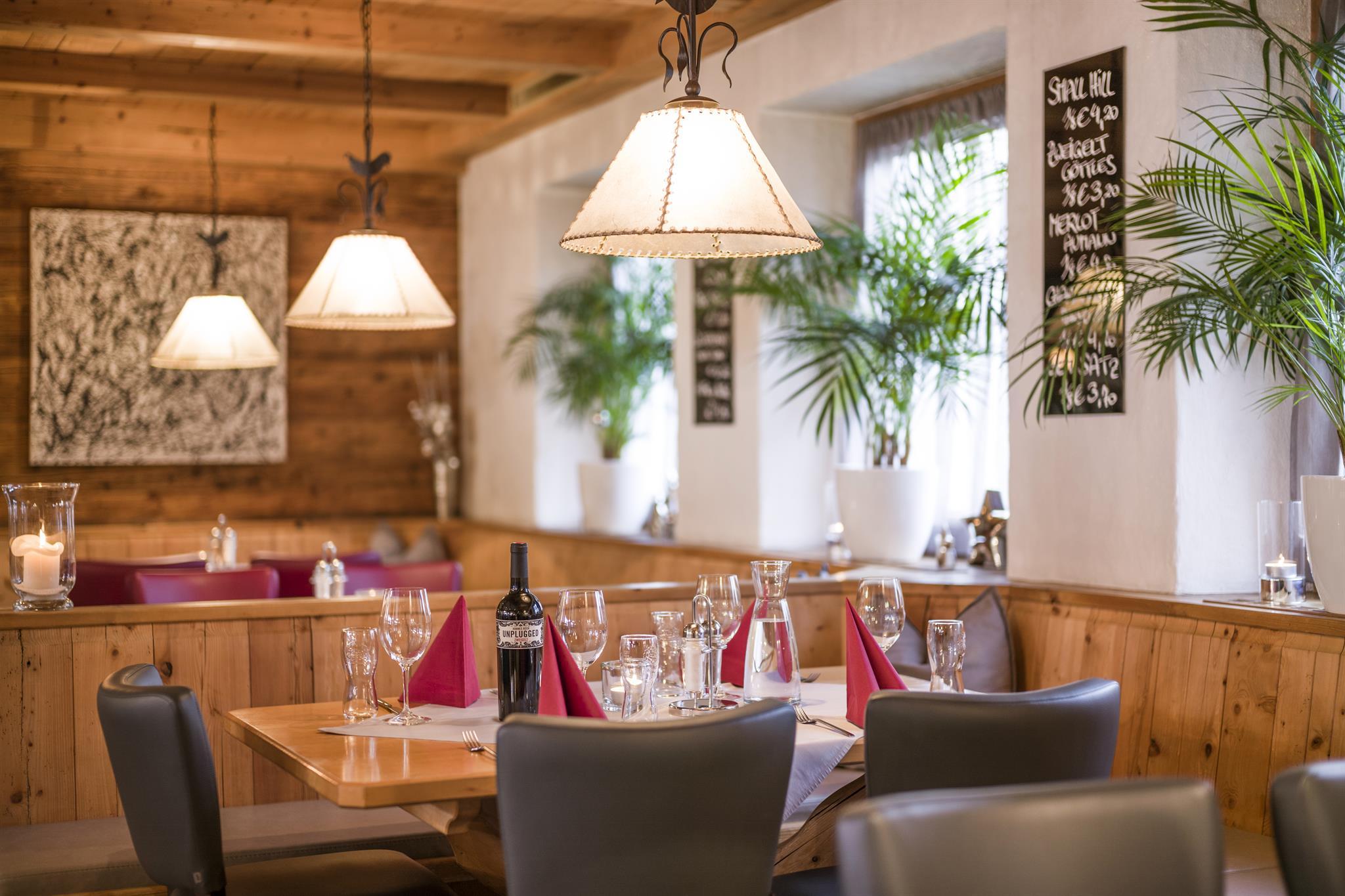 Ein gemütlicher Restaurantraum mit Holzdecke, Lampen, Tafel und gedecktem Tisch mit Wein und Gläsern.