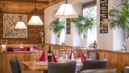 Ein gemütlicher Restaurantraum mit Holzdecke, Lampen, Tafel und gedecktem Tisch mit Wein und Gläsern.