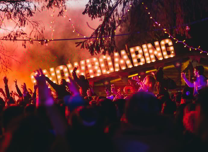 The image shows a celebrating crowd at the forest festival grounds against a black and pink background.