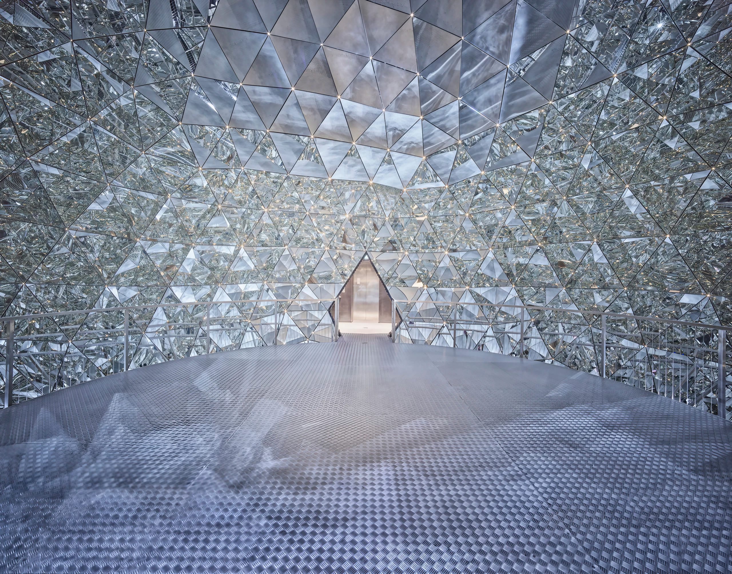 Innenansicht eines futuristischen, spiegelnden Gebäudes mit geometrischen Mustern und reflektierenden Flächen.
