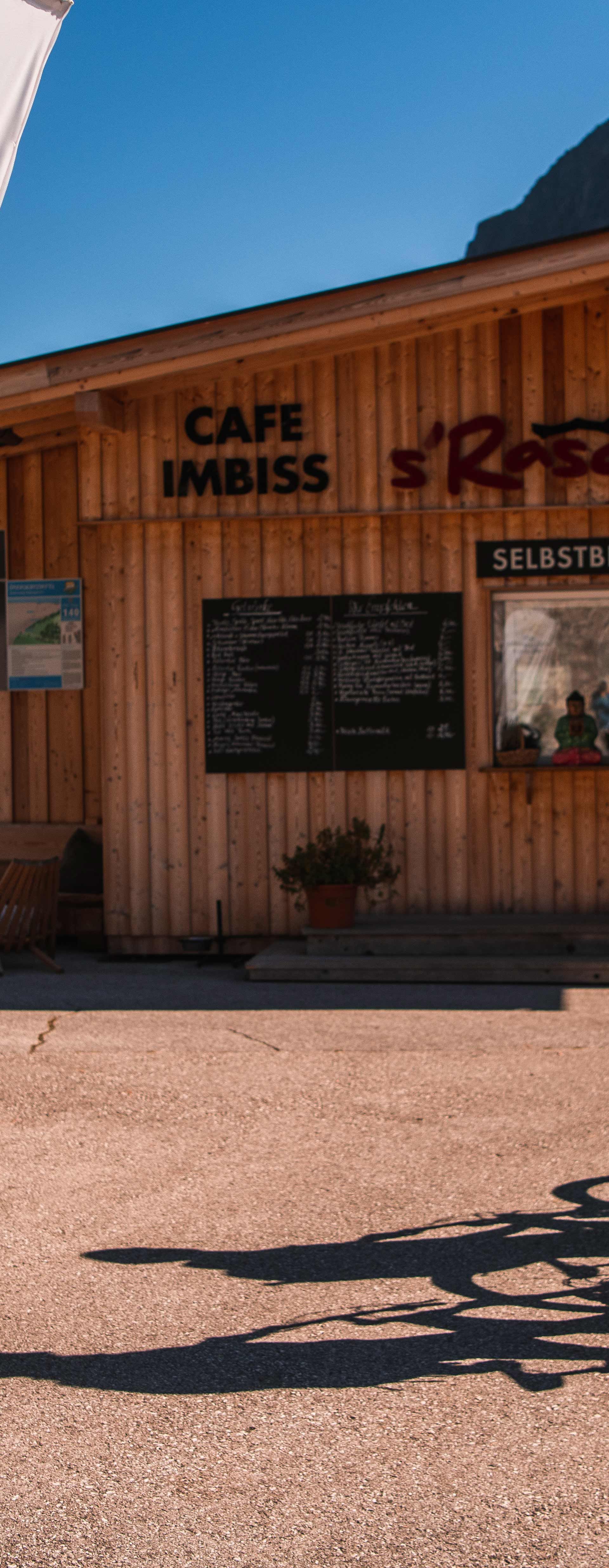 Two e-bikers in front of an e-bike charging station in the Mayrhofen-Hippach holiday region on a sunny day, with an info point and mountain scenery in the background.