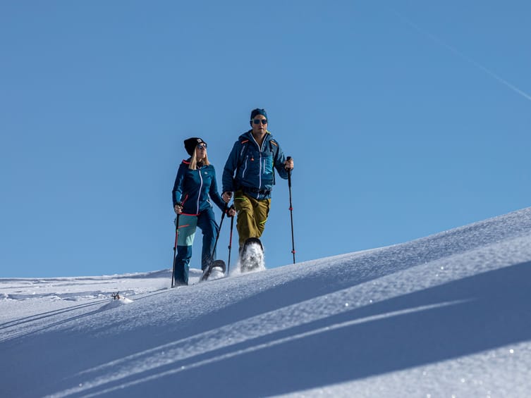 Zwei Personen beim Schneeschuhwandern in Mayrhofen-Hippach auf einem sonnigen Hang mit unberührtem Schnee und Blick in die Winterlandschaft.