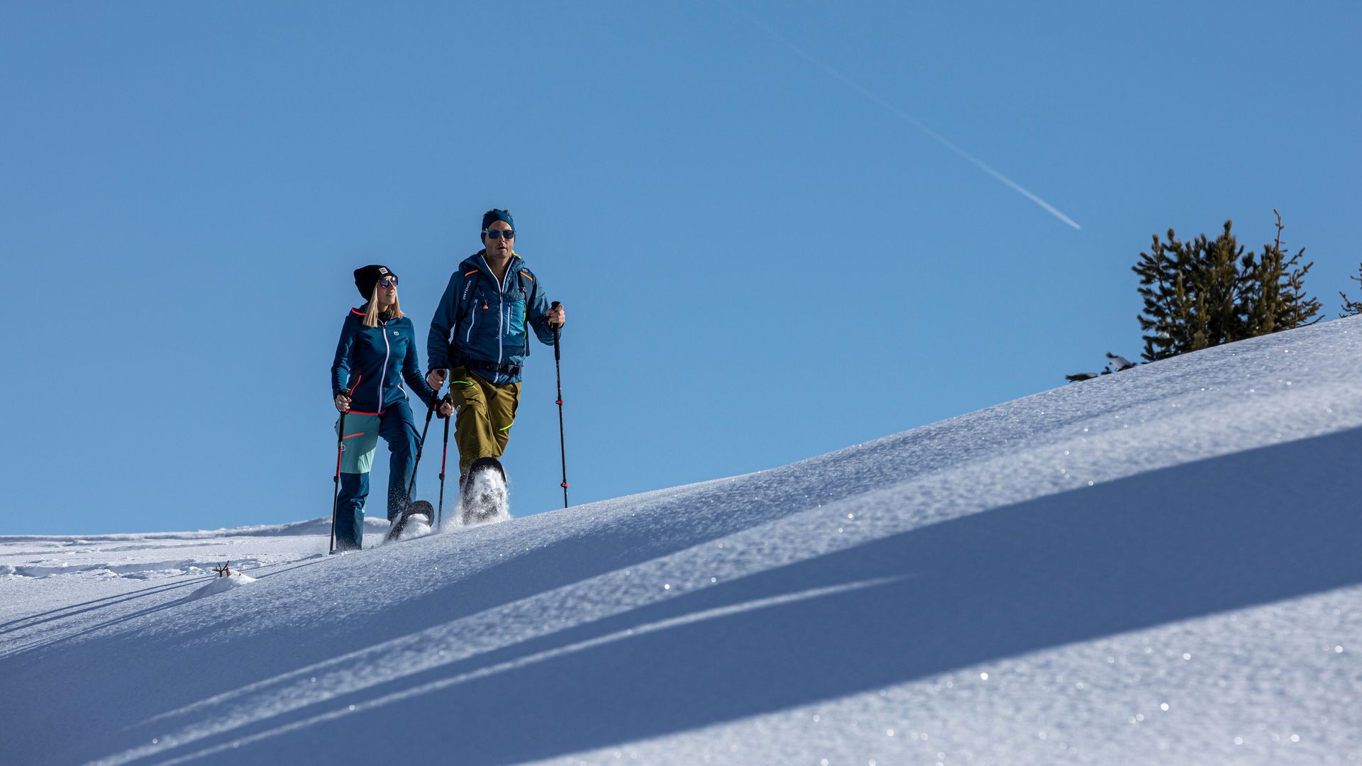 Two people enjoying a snowshoe hike in Mayrhofen-Hippach, walking across a sunny slope with untouched winter snow and mountain scenery.