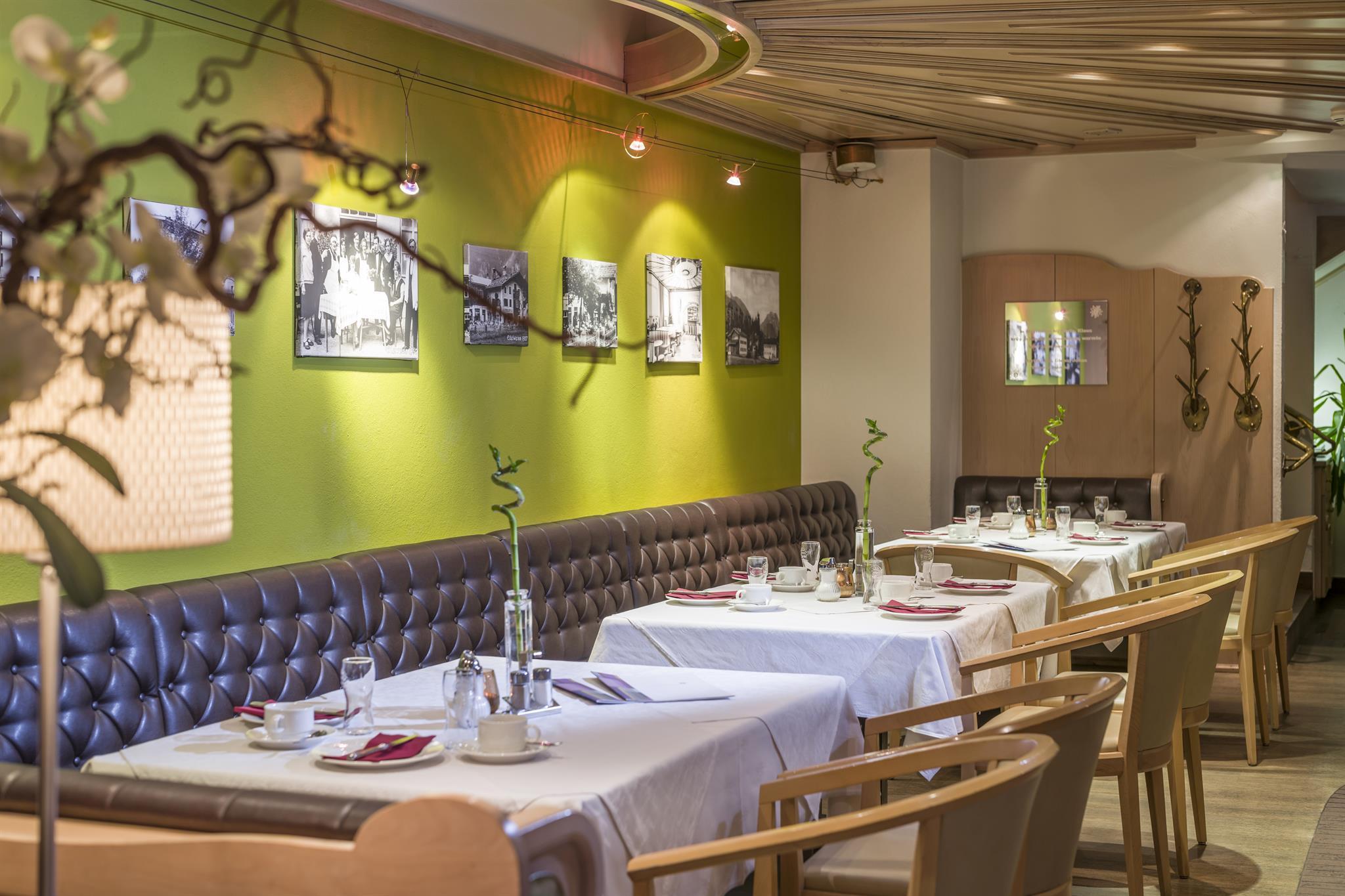 Ein gemütlicher Restaurantraum mit grüner Wand, Fotos, Tischen mit weißen Tischdecken und Stühlen.