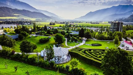 A beautiful garden with a carousel, surrounded by green trees and colorful flowers, with mountains in the background.