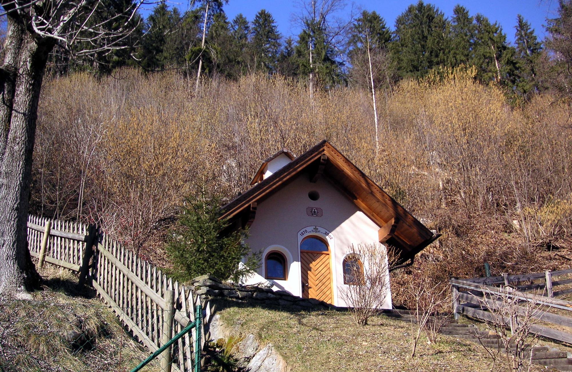 Village chapel in Schwendau with white facade and wooden shingle roof, surrounded by a fence and meadows at the forest edge, Station 10 of the Schwendau Trail “Village Chapel,” photographed by the municipality of Schwendau.
