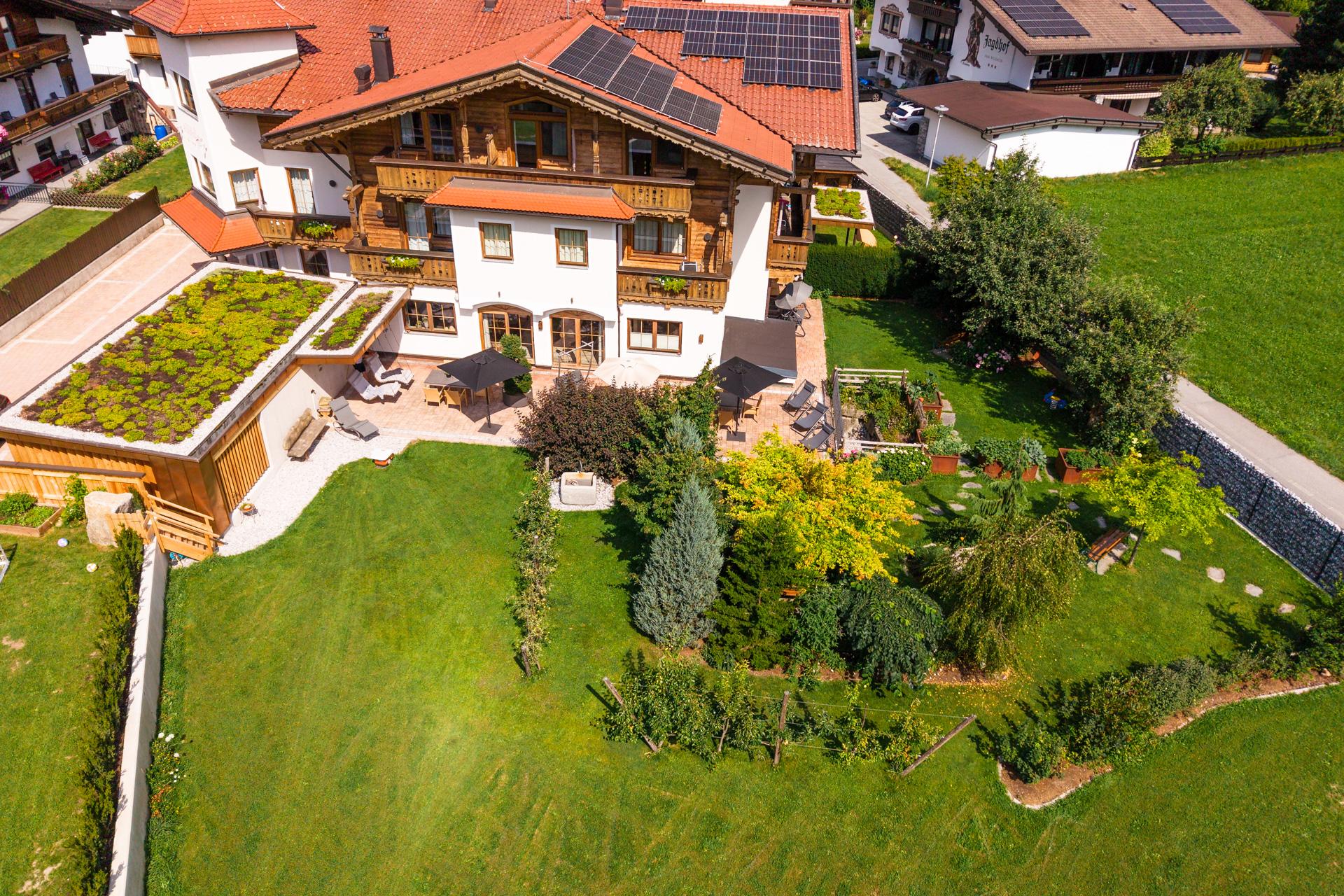 Häuser mit Gärten und Solarpanelen auf dem Dach, grüne Wiesen und Bäume im Vordergrund, sonniger Tag.