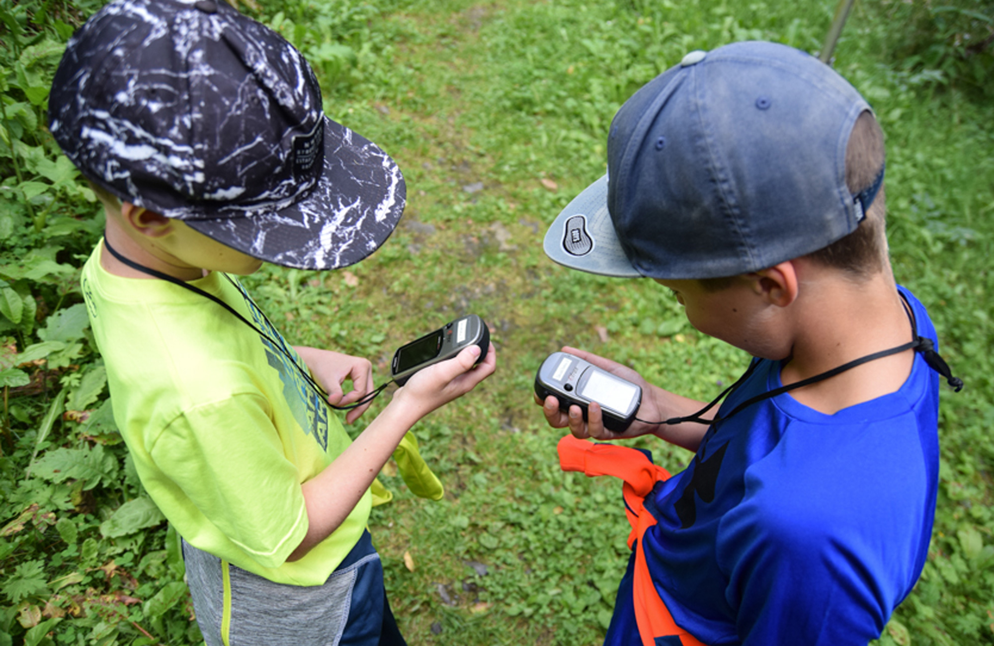 Zwei Kinder mit Kappen stehen auf einem Waldweg in Ginzling, Zillertal. Sie halten ein GPS-Gerät und einen Kompass in den Händen und suchen nach einem Geocache.