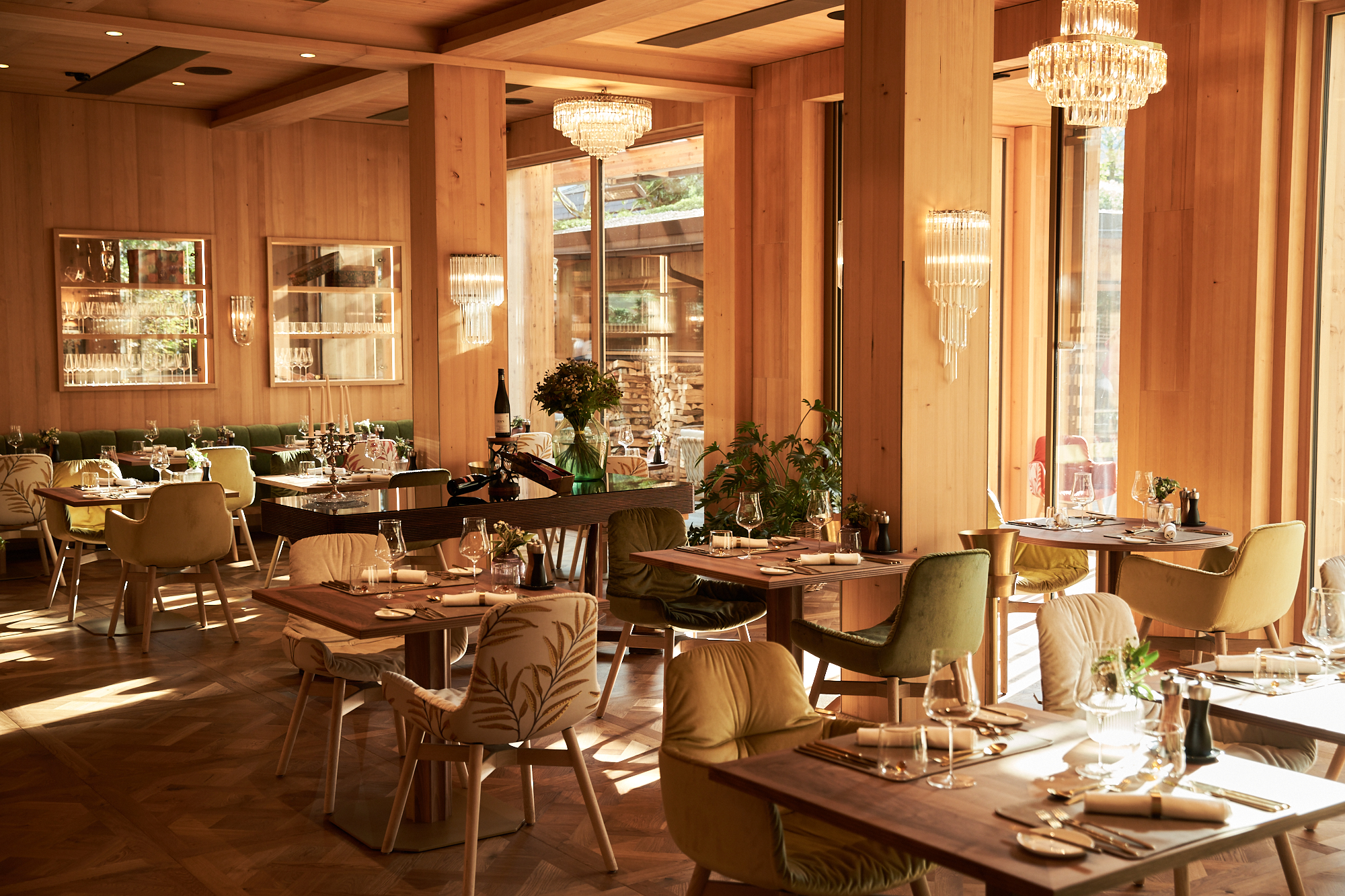 Elegant restaurant with wood decor, large windows, chandeliers, and well-set tables.
