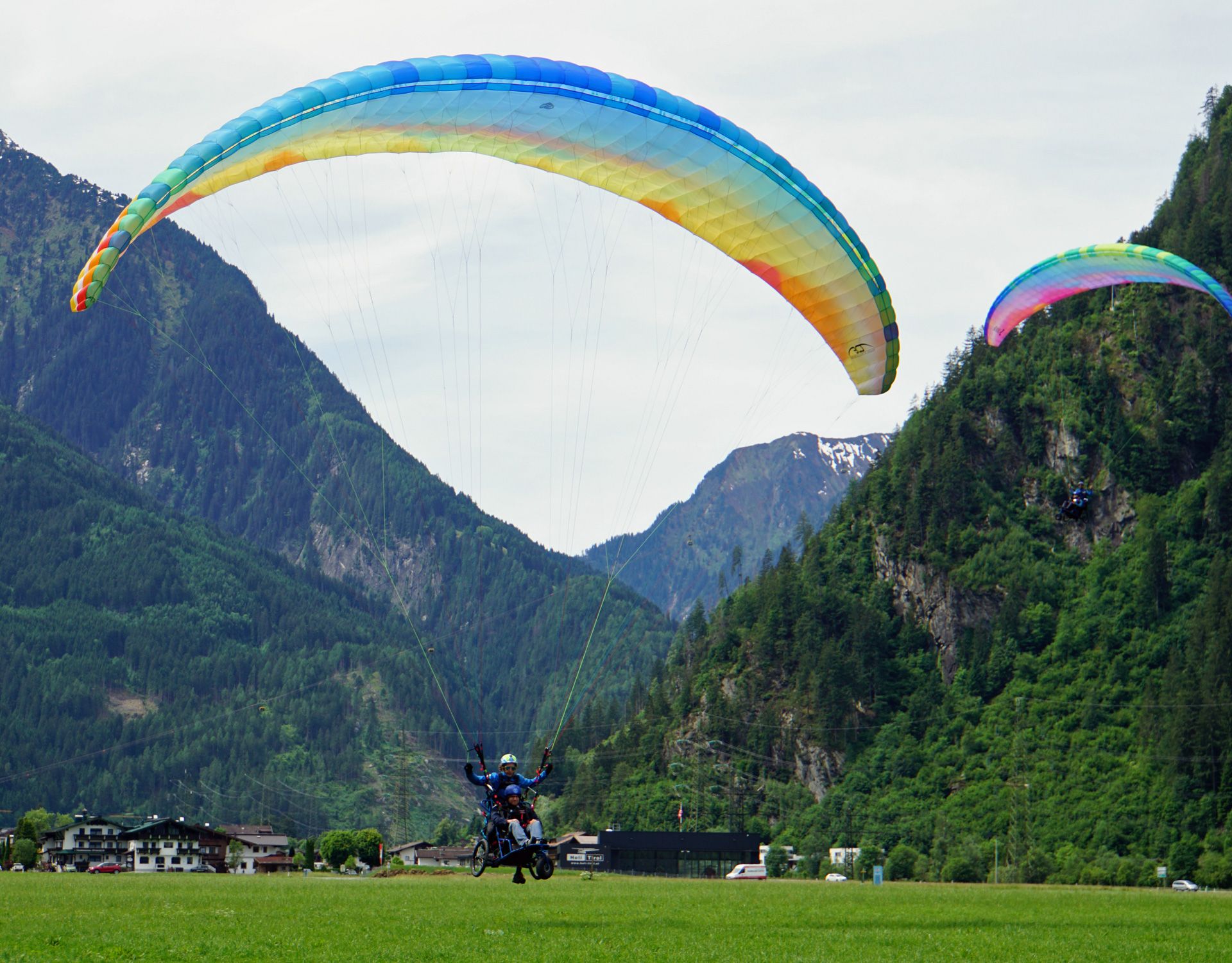 A pilot in wheelchair-supported paragliding lands on a green meadow in Mayrhofen, Zillertal, with a stunning Alpine backdrop.