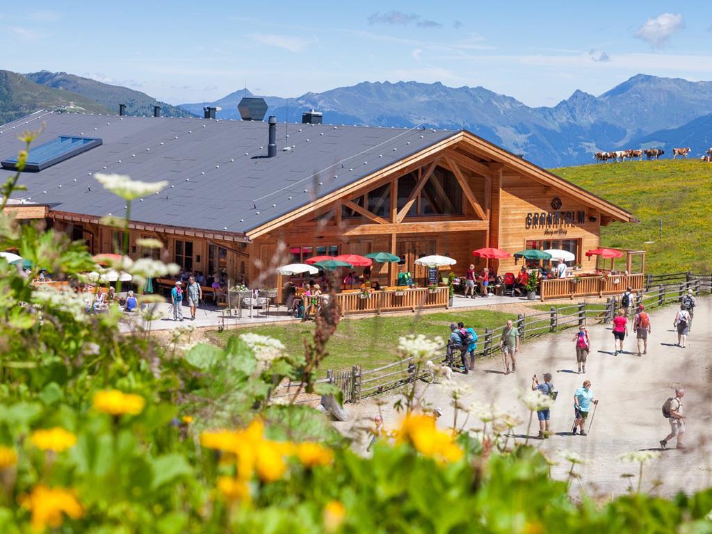 The image shows an exterior view of the Granatalm in summer, with a meadow of flowers in the foreground.