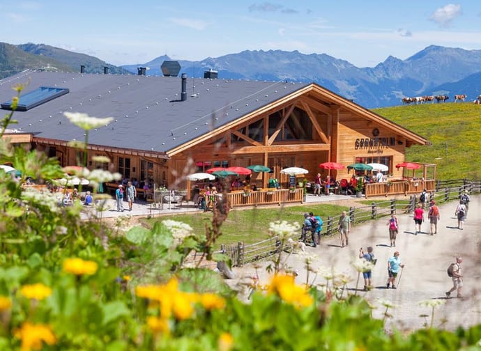 The image shows an exterior view of the Granatalm in summer, with a meadow of flowers in the foreground.