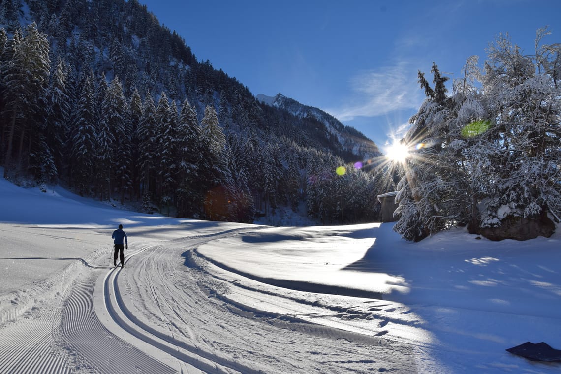 Langlaufloipe in Ginzling Langläufer auf der gespurten Langlaufloipe in Ginzling, die durch das verschneite Tal mit Wald und Sonne im Hintergrund führt.