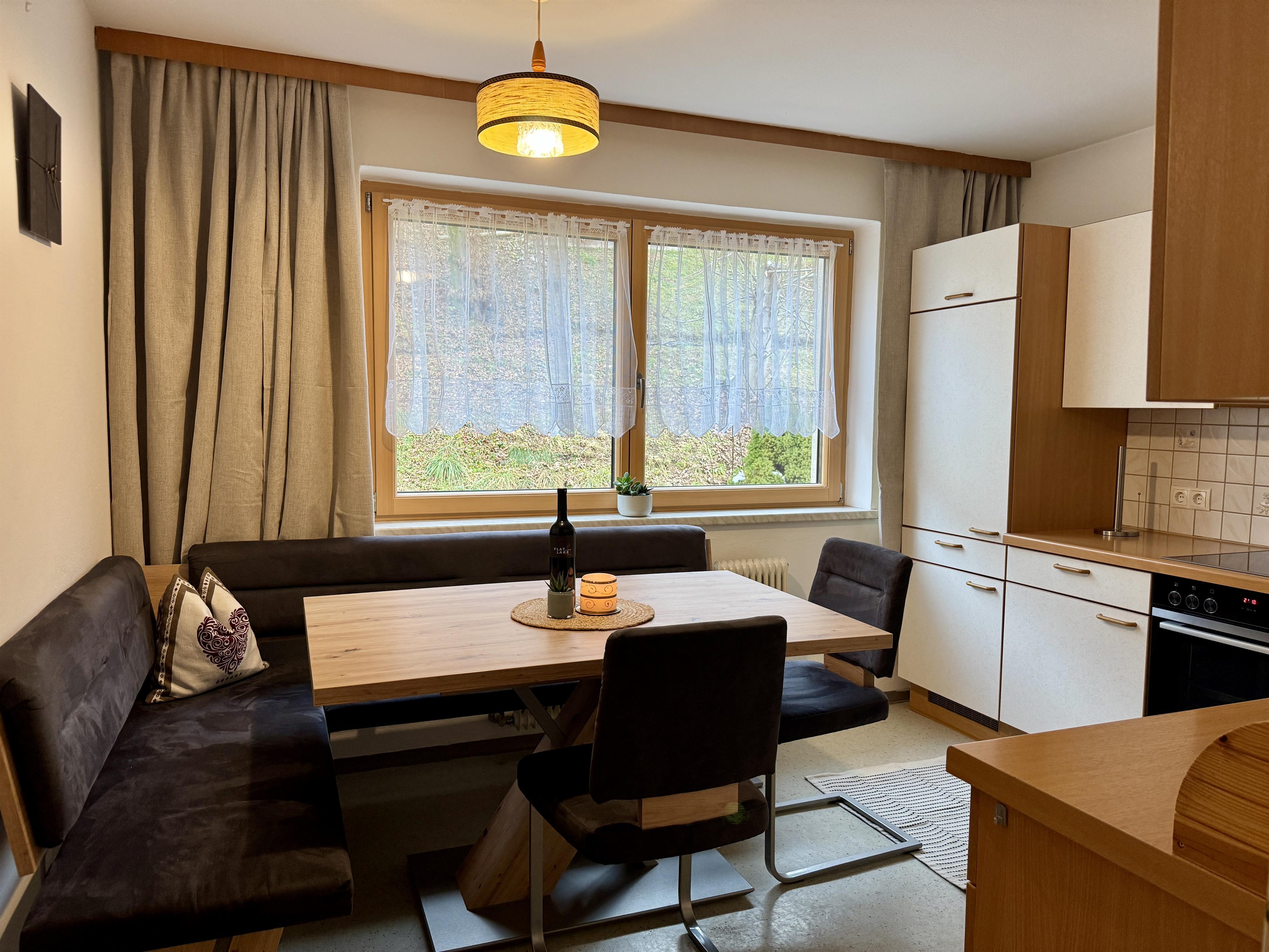 A bright kitchen with a dining table, black chairs, large windows, and beige curtains.