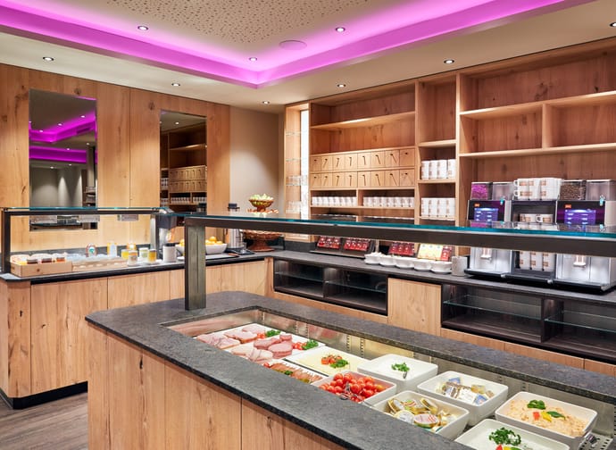 Breakfast buffet with fresh food, wooden shelves, and pink-lit ceiling in a modern setting.