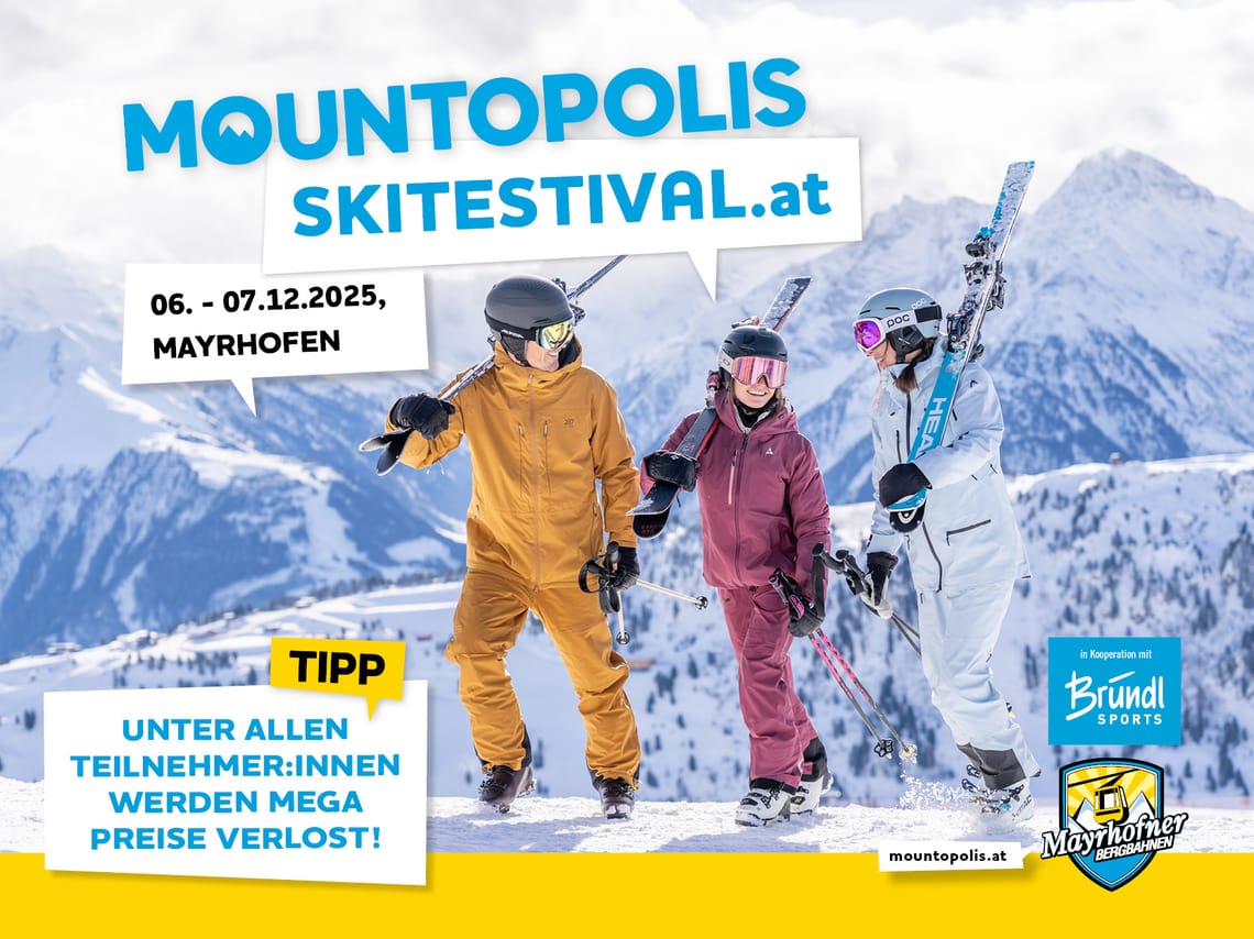 Three skiers in colorful gear on snowy mountain with mountain peaks behind them.