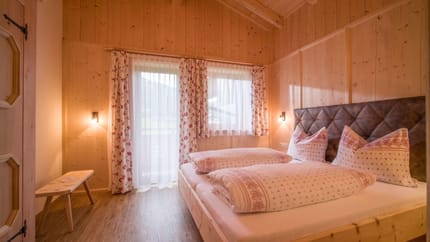 A cozy bedroom with wooden walls, bed, curtains, and soft lighting, warm and inviting.