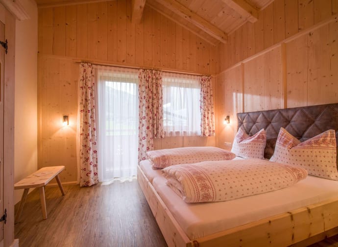 Ein gemütliches Schlafzimmer mit Holzverkleidung, Bett, Vorhängen und weichem Licht, warm und einladend.